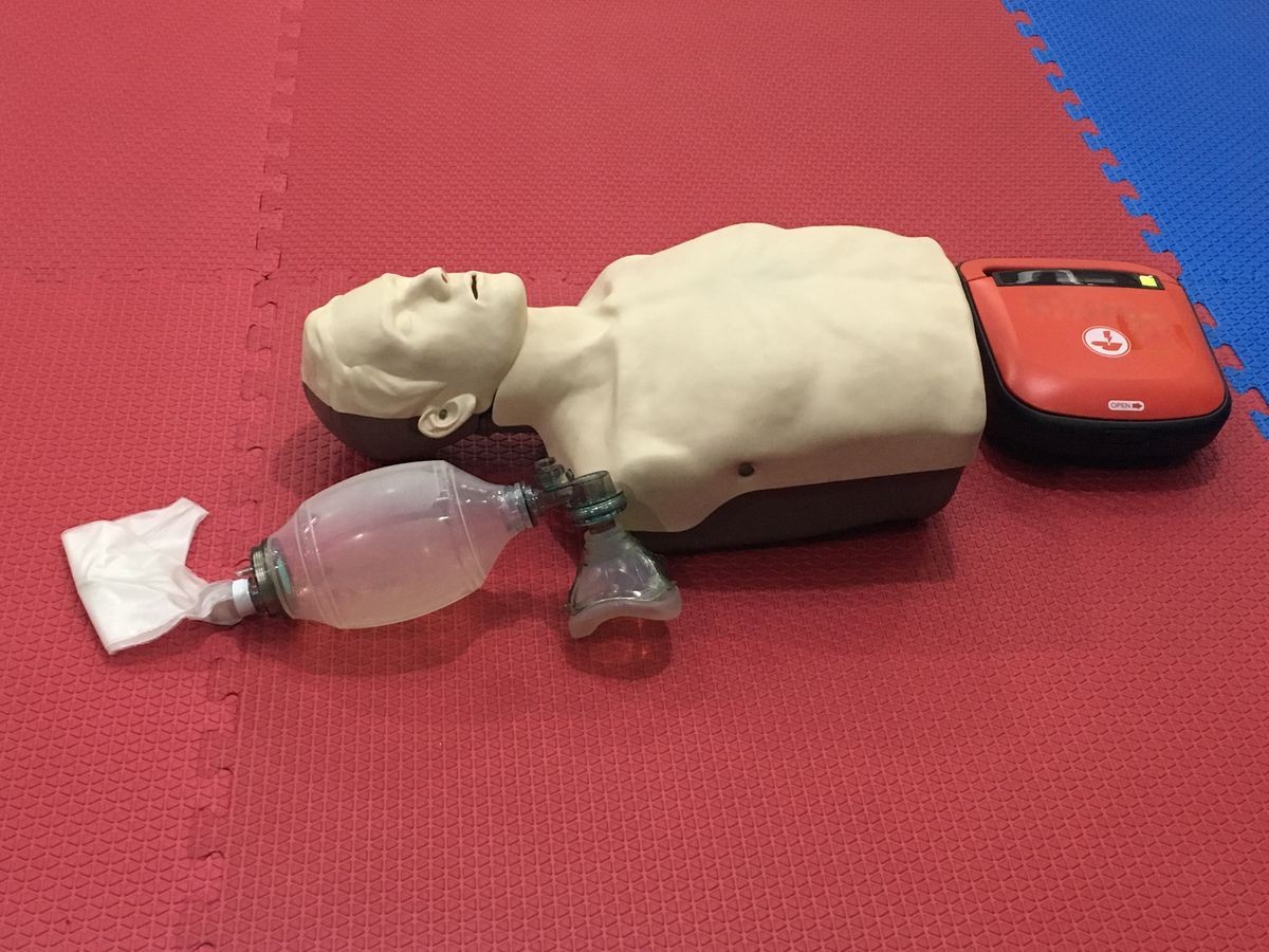 Adult cpr training model, mask with bag and AED on red and blue carpet in simulation room